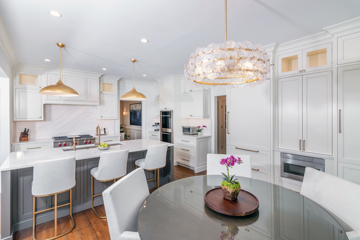 White kitchen cabinets with large gold light fixtures and a table