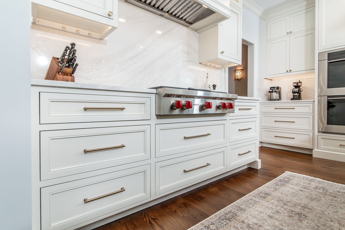 A white kitchen with white cabinetry and a white backsplash with wood flooring