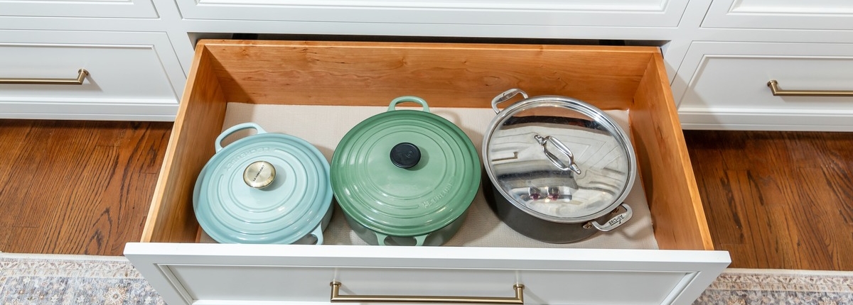 A kitchen with a white deep cabinet drawer pulled out full of pots and pans