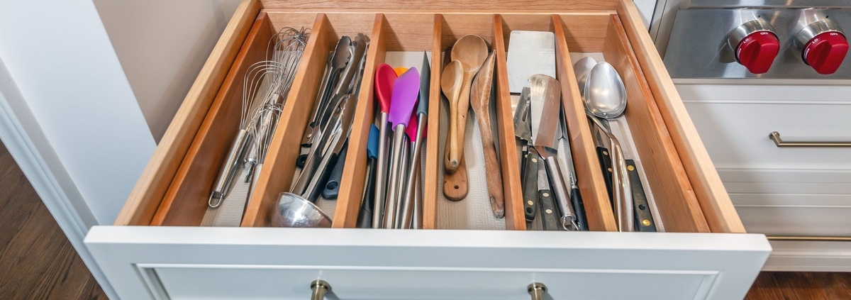 A kitchen with a custom white cabinet drawer pulled out full of organized utensils