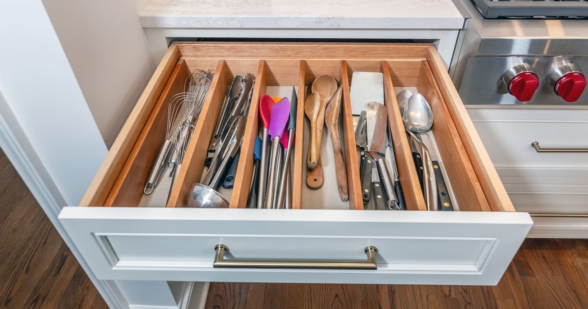 A kitchen with a custom white cabinet drawer pulled out full of organized utensils