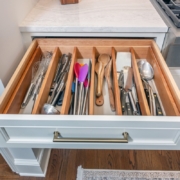 A kitchen with a custom white cabinet drawer pulled out full of organized utensils