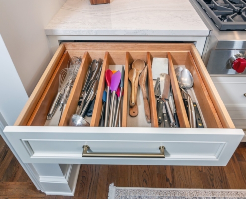 A kitchen with a custom white cabinet drawer pulled out full of organized utensils