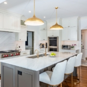 A white kitchen with a marble island countertop with grey cabinetry