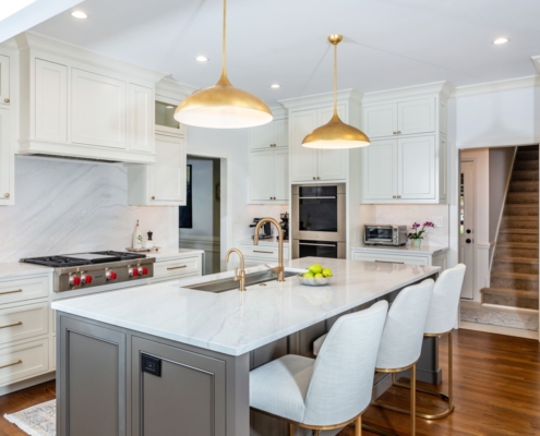 A white kitchen with a marble island countertop with grey cabinetry