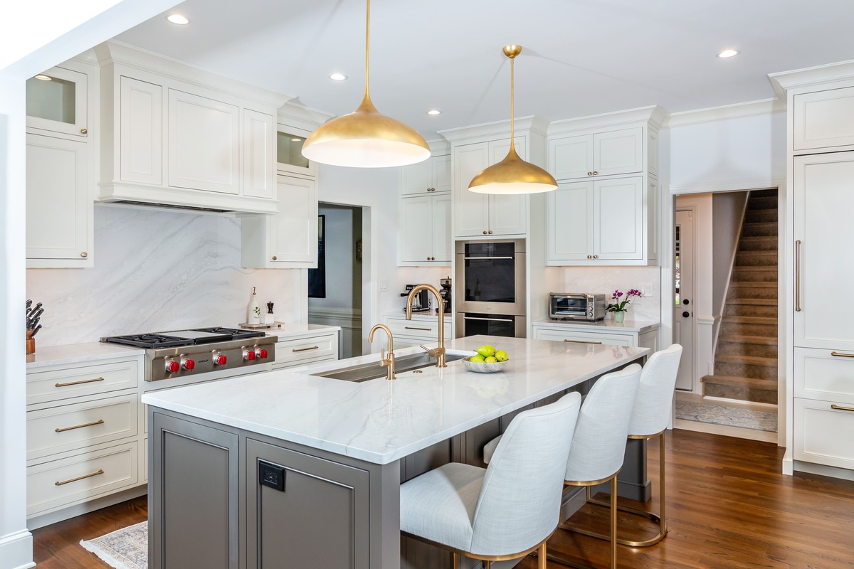 A white kitchen with a marble island countertop with grey cabinetry