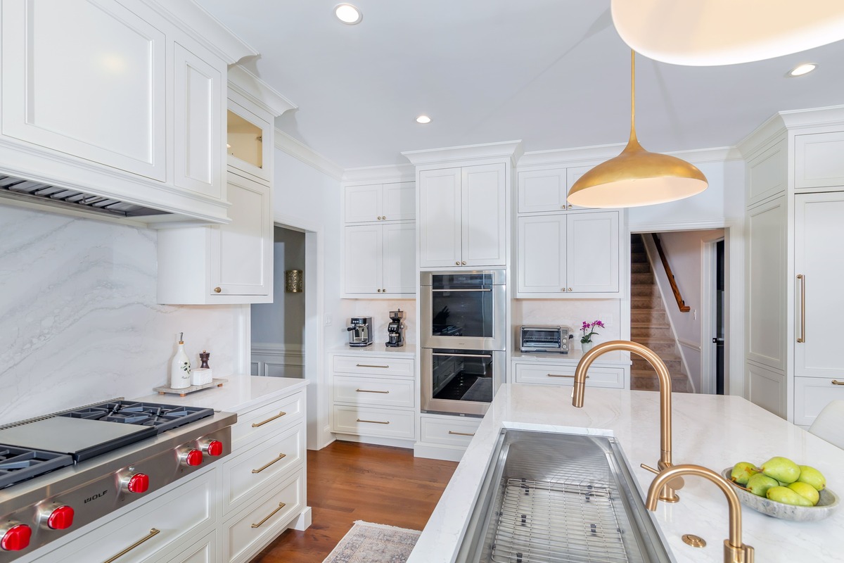 A large white kitchen with white cabinetry and a double sided gold faucet with wood flooring