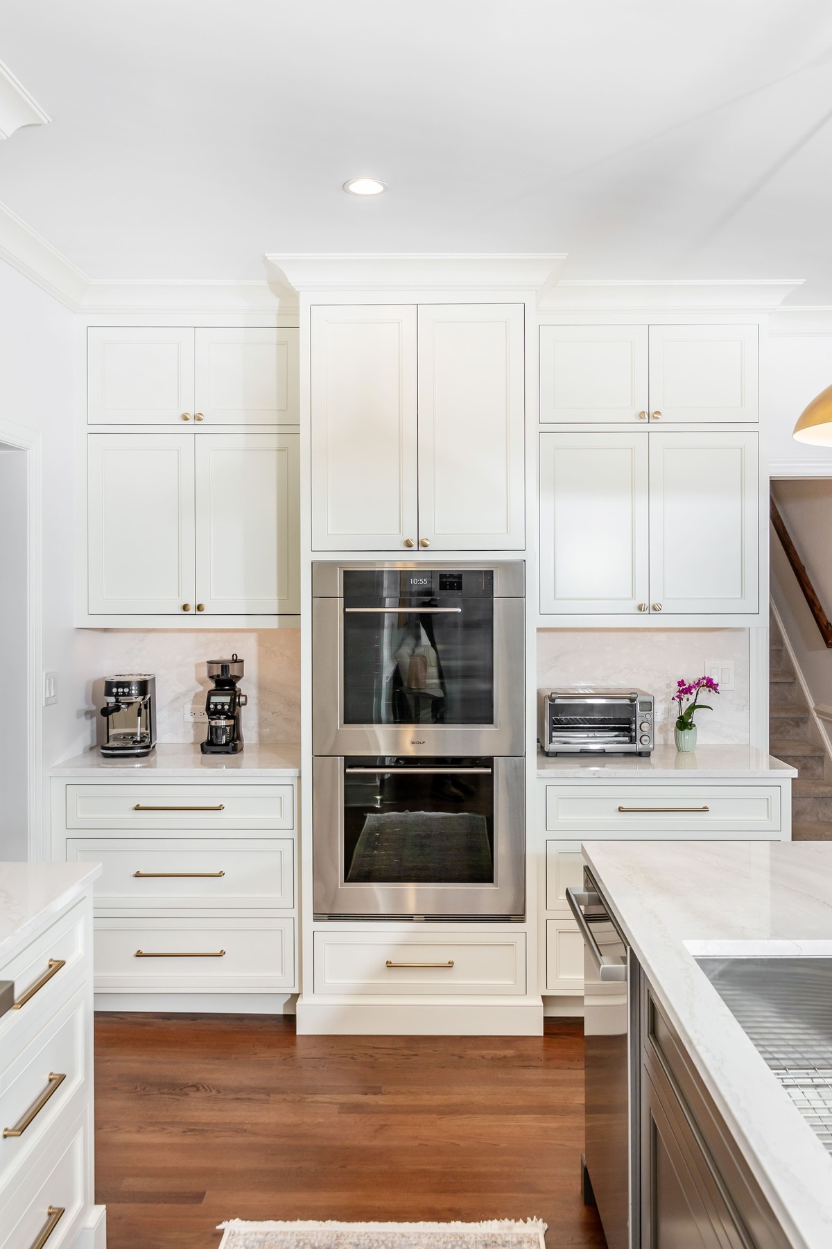 A white kitchen with a double stacked microwave and oven and wood flooring