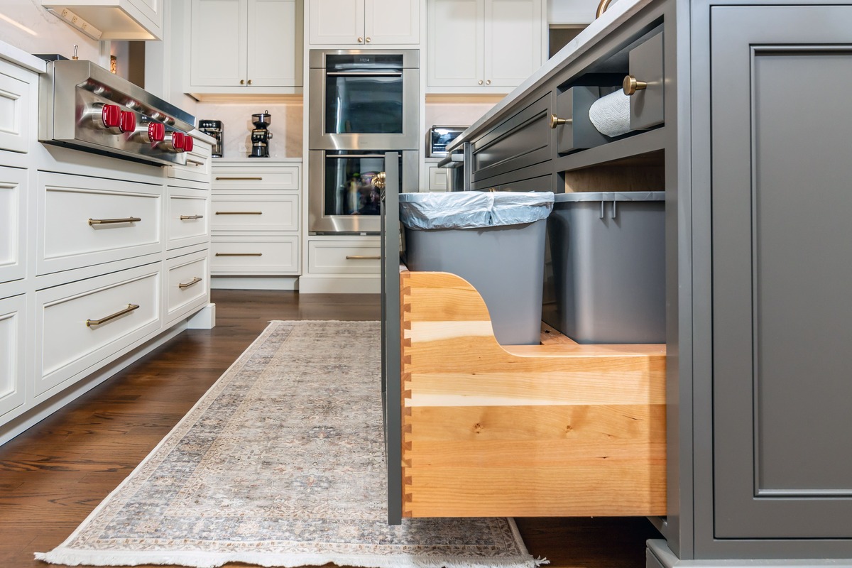 A kitchen with white and grey cabinetry and a pull out double trash can cabinet drawer