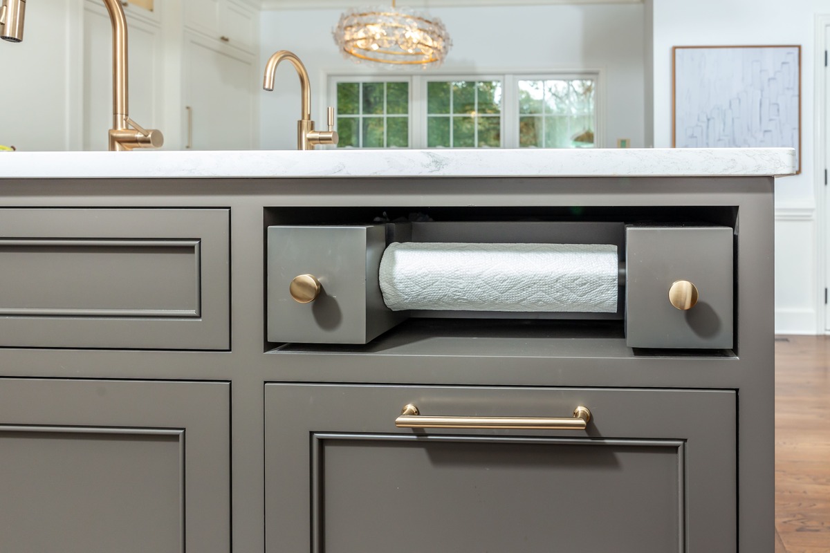 A kitchen with grey cabinetry and a paper towel holder inside the island countertop