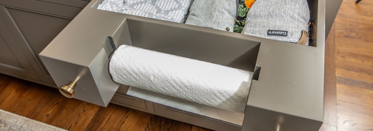 A kitchen with grey cabinets a pull out paper towel holder with a storage drawer behind it