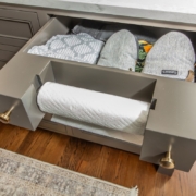 A kitchen with grey cabinets a pull out paper towel holder with a storage drawer behind it