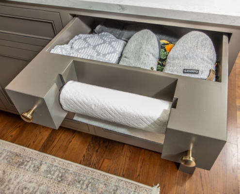 A kitchen with grey cabinets a pull out paper towel holder with a storage drawer behind it