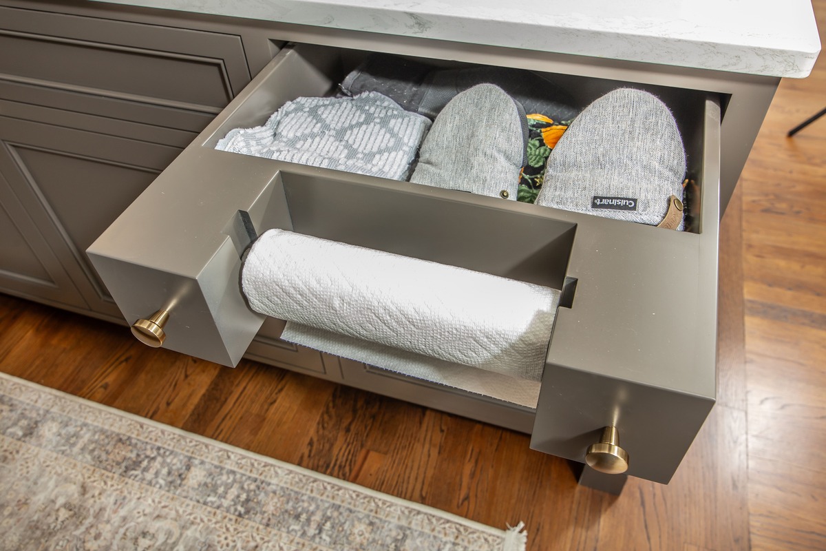 A kitchen with grey cabinets a pull out paper towel holder with a storage drawer behind it