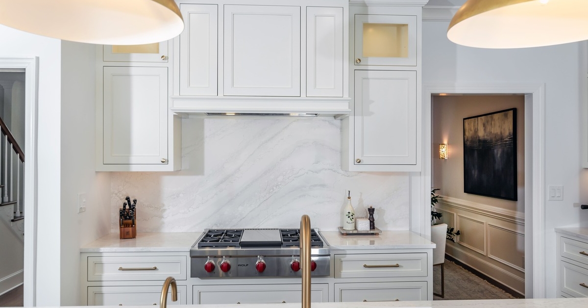 A white kitchen with a white backsplash and a double sided bronze sink with gold lighting
