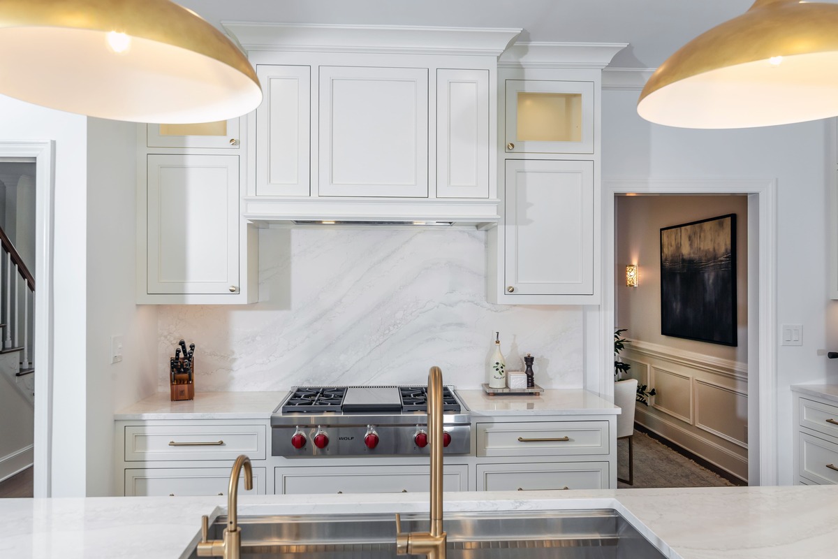 A white kitchen with a white backsplash and a double sided bronze sink with gold lighting