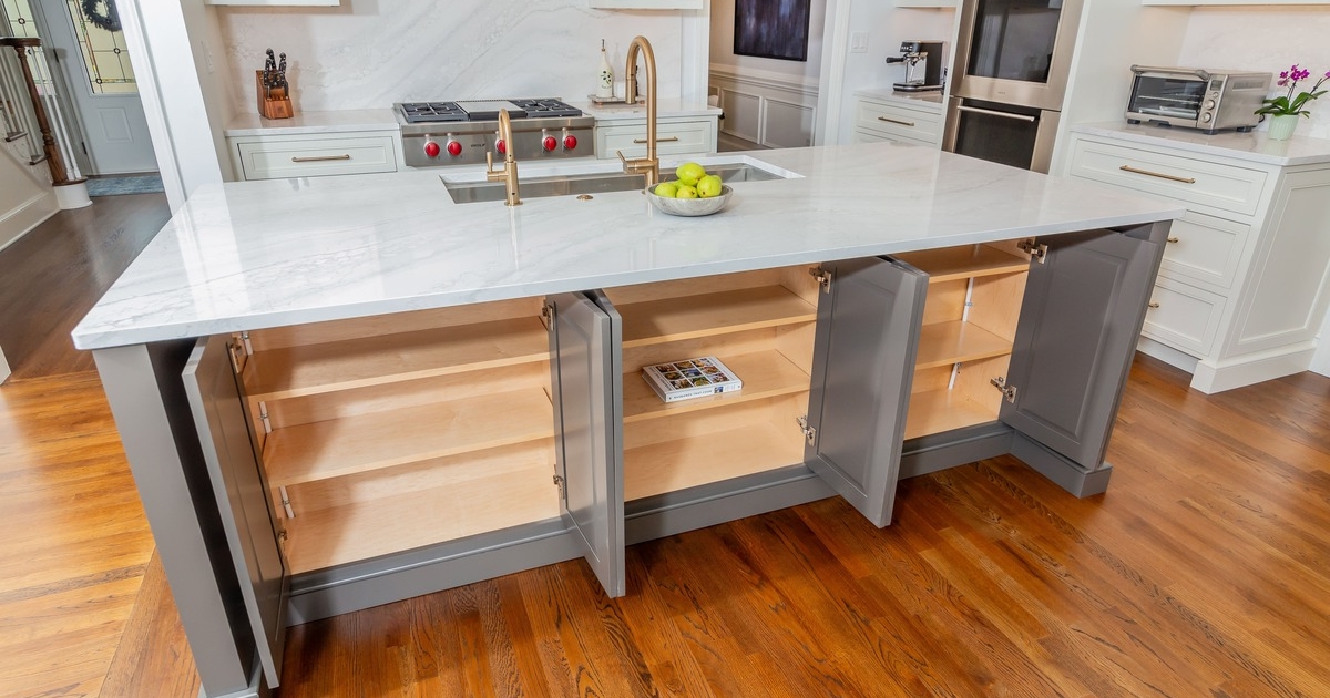 A kitchen with a large marble island countertop with grey storage cabinets built in
