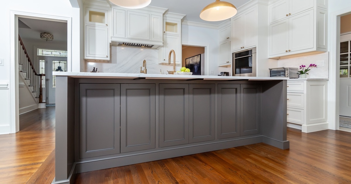 A large white kitchen with a large grey island countertop with wood flooring