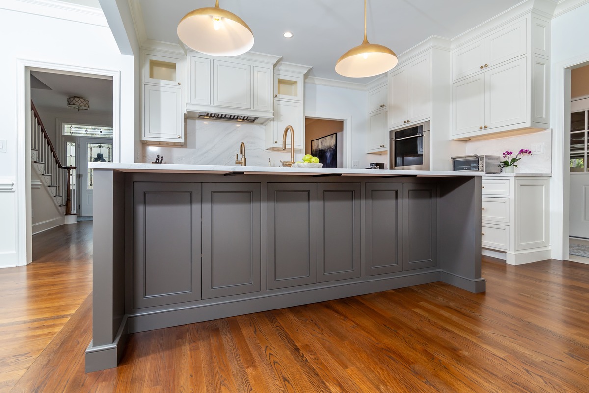 A large white kitchen with a large grey island countertop with wood flooring