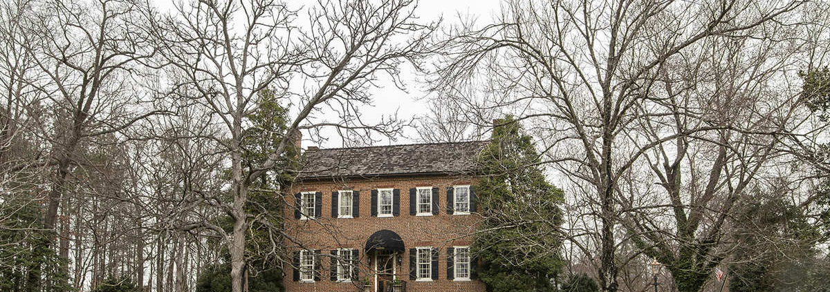 Historical home with black shutters and large trees