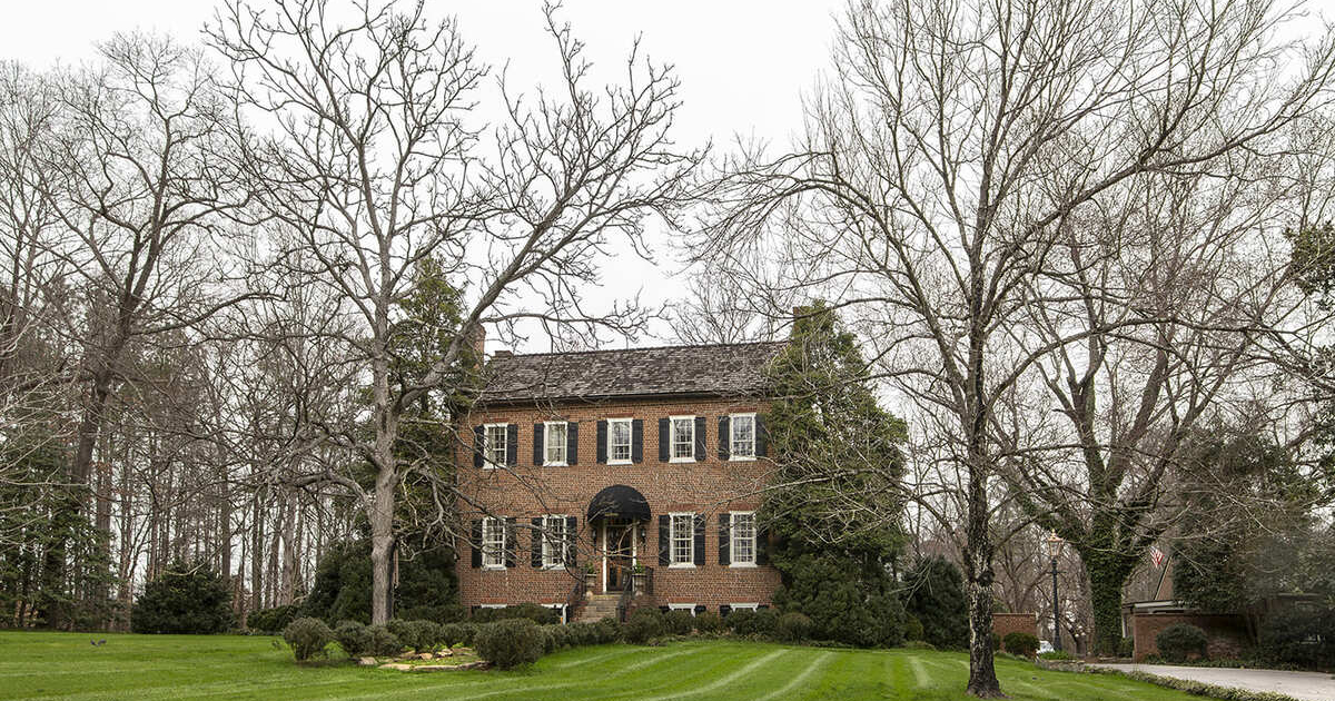 Historical home with black shutters and large trees