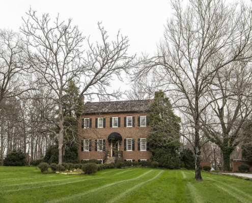 Historical home with black shutters and large trees