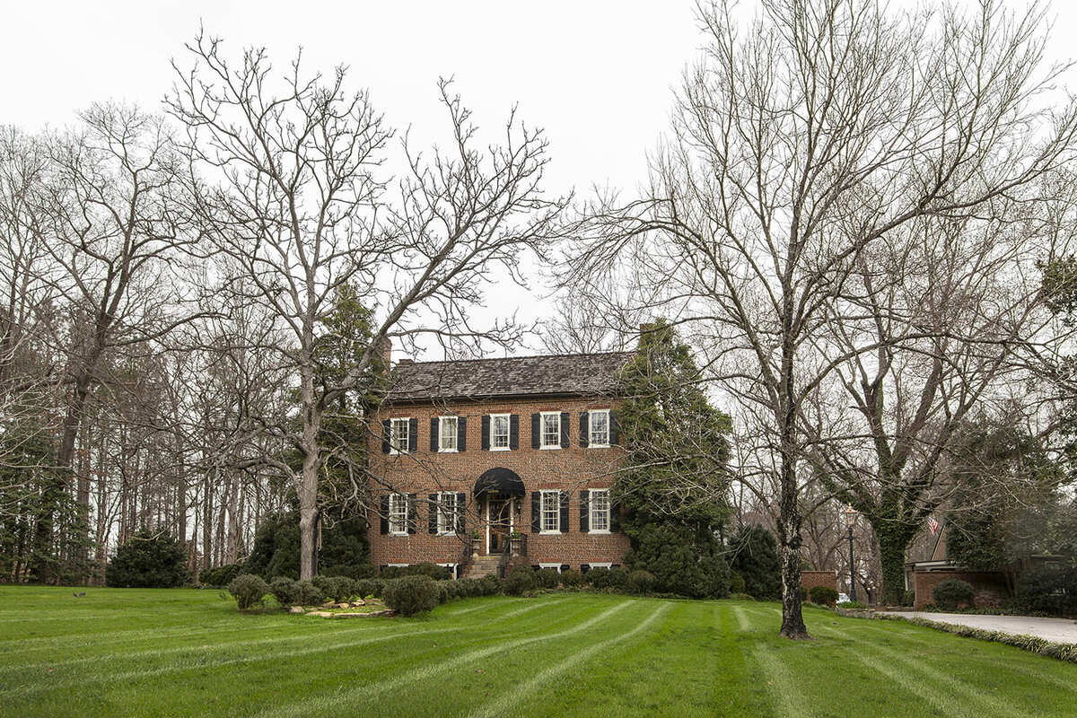 Historical home with black shutters and large trees