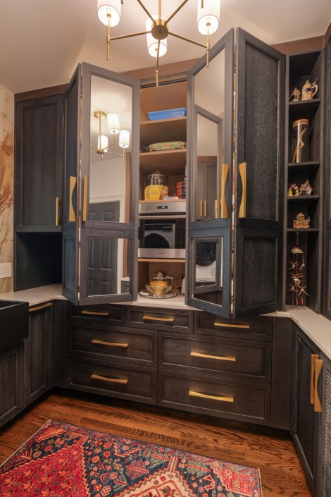 A butler pantry with black cabinetry with bi-fold cabinet doors and gold hardware