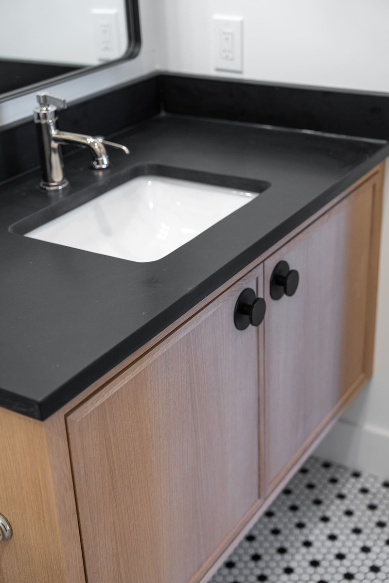 A bathroom with a wooden floating vanity with a black countertop and a sink