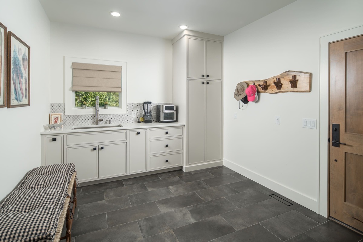 A open style laundry room with white cabinets and black and grey tile flooring