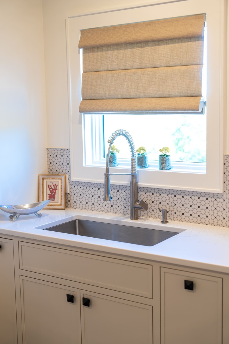 A laundry room with white cabinets and a white countertop with a sink