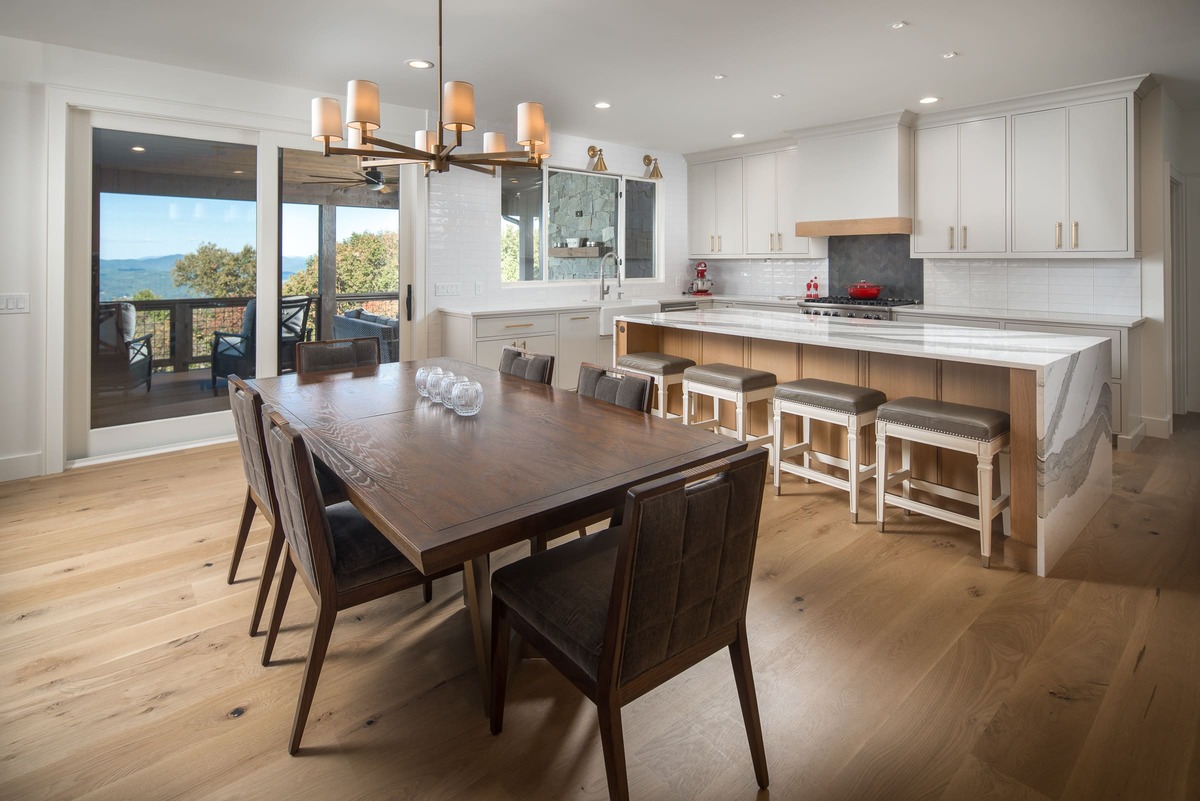 A kitchen with white cabinets a large dining table and a island countertop with barstools