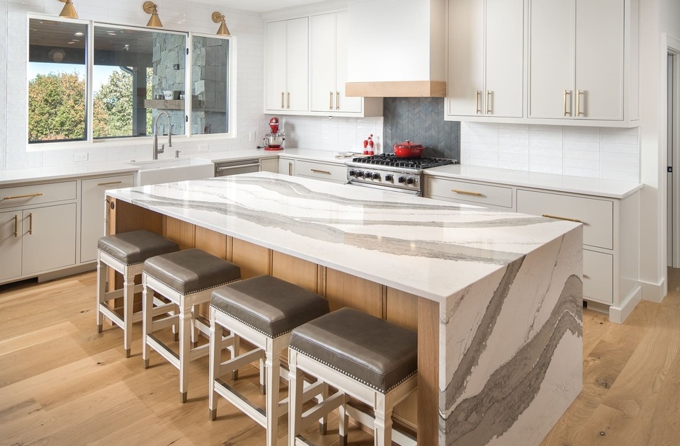 A kitchen with white cabinets a large kitchen island with barstools and wood flooring