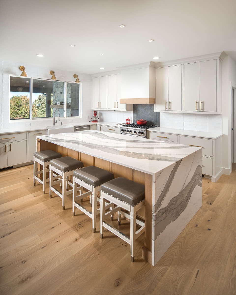 A kitchen with white cabinets a large kitchen island with barstools and wood flooring