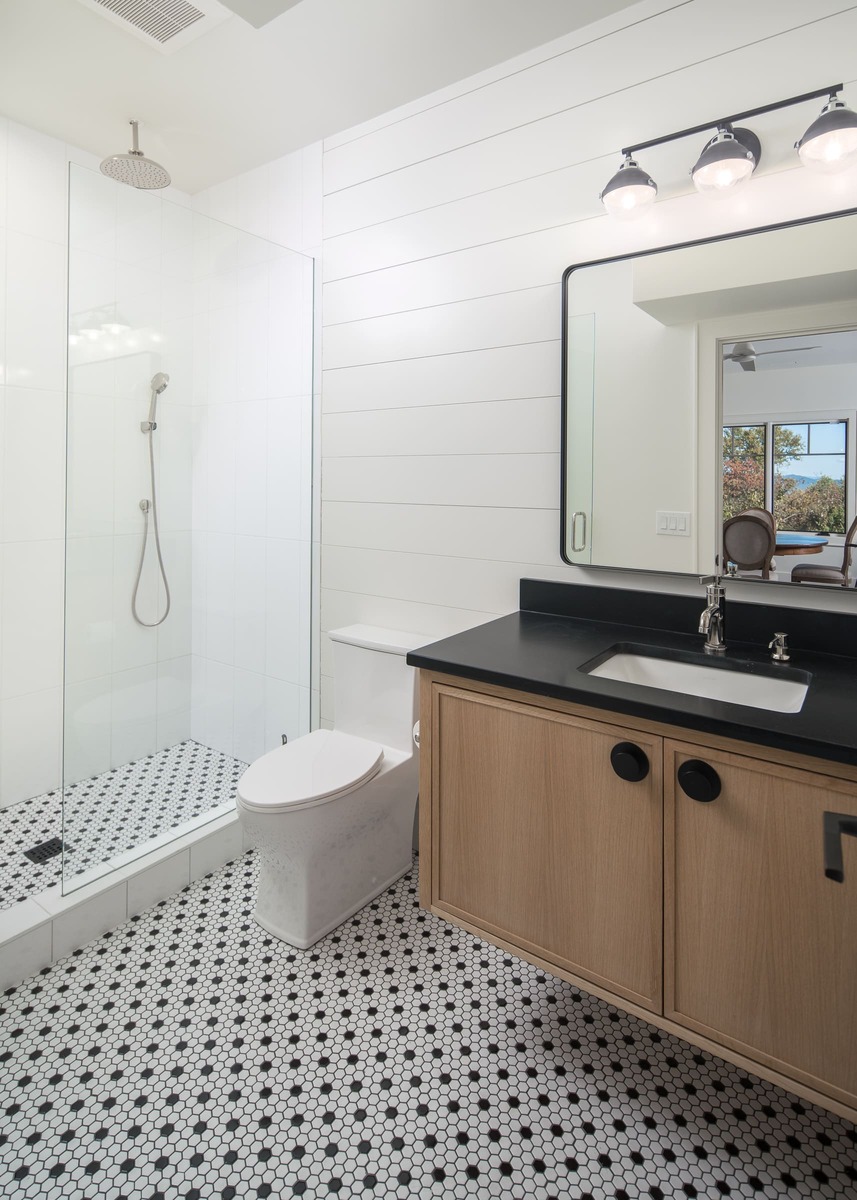 A bathroom with brown cabinetry and a black countertop with custom flooring and a shower