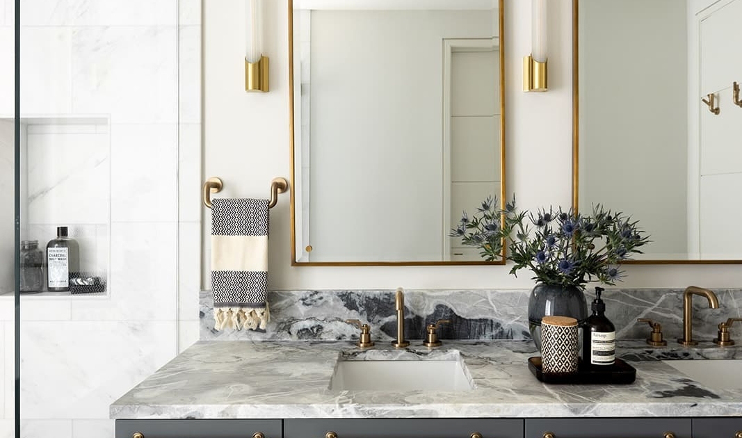 A bathroom with gray cabinets and a floating vanity with gold hardware and mirrors