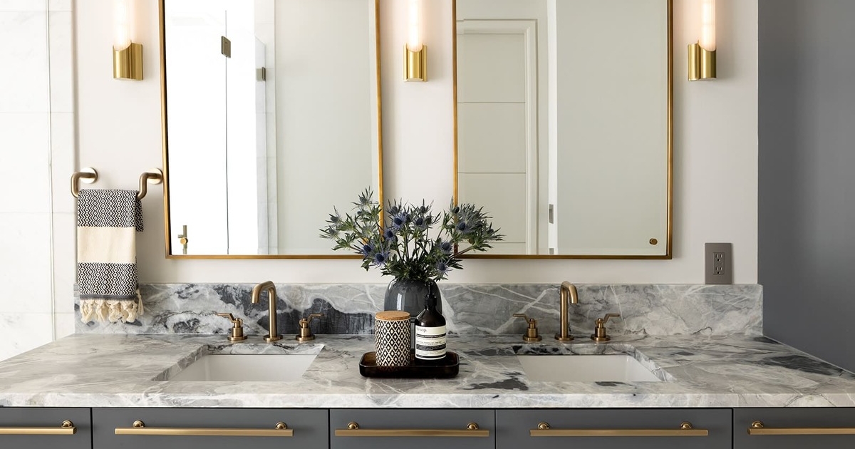 A bathroom with gray cabinetry with gold hardware and gold mirrors and decor