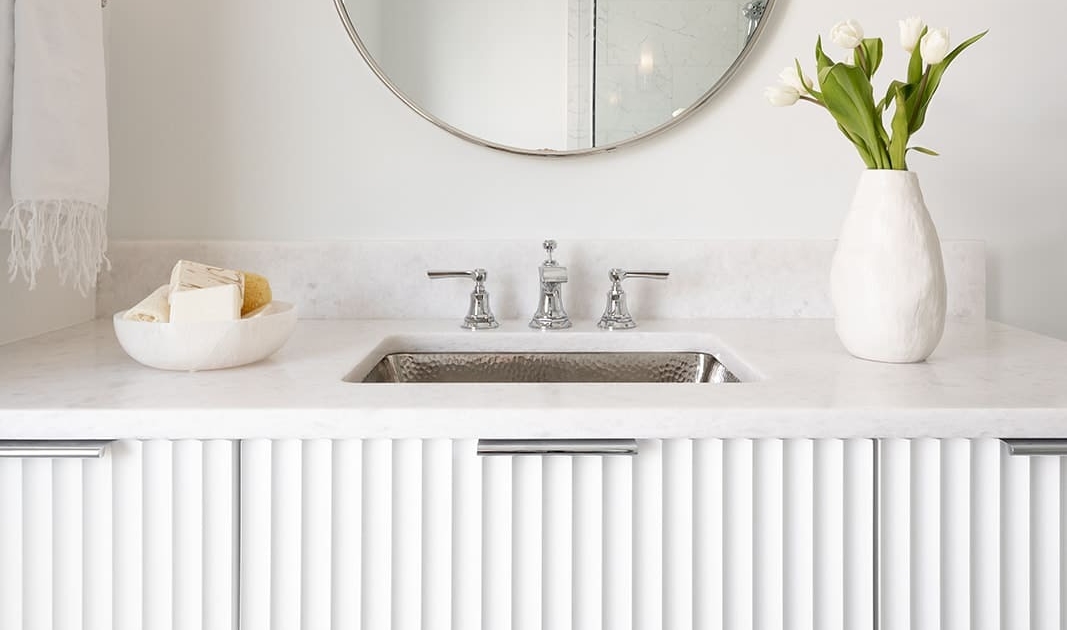 A white bathroom with a floating vanity with fluted cabinet doors and decor lighting