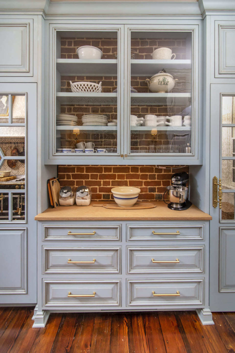 A kitchen with custom cabinets with glass cabinet doors and a brick background