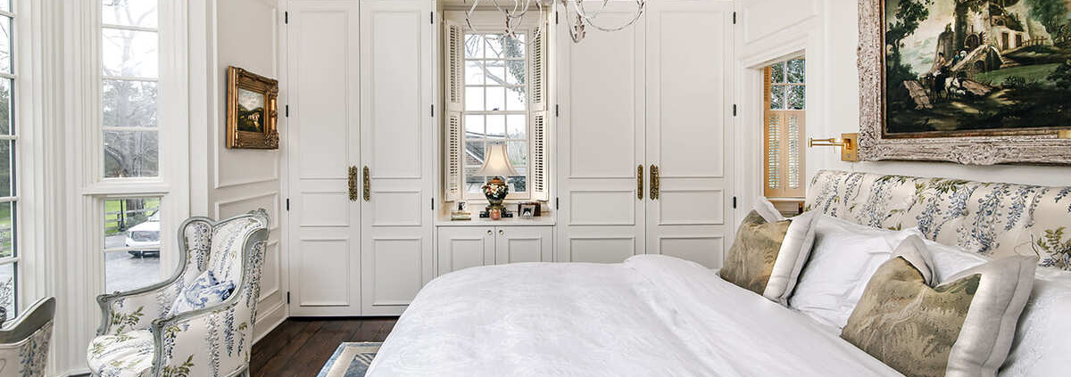 A master bedroom with white cabinetry and a built in closet on both sides and a white bed