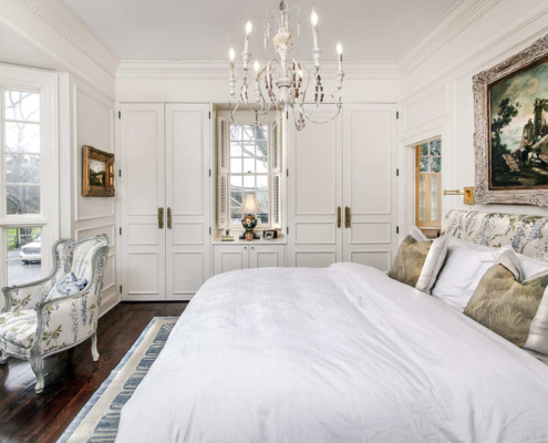 A master bedroom with white cabinetry and a built in closet on both sides and a white bed