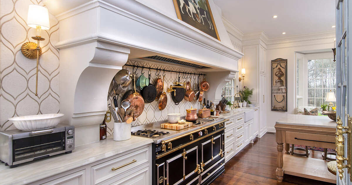 Large white kitchen hood with pot and pan hooks and a large stove