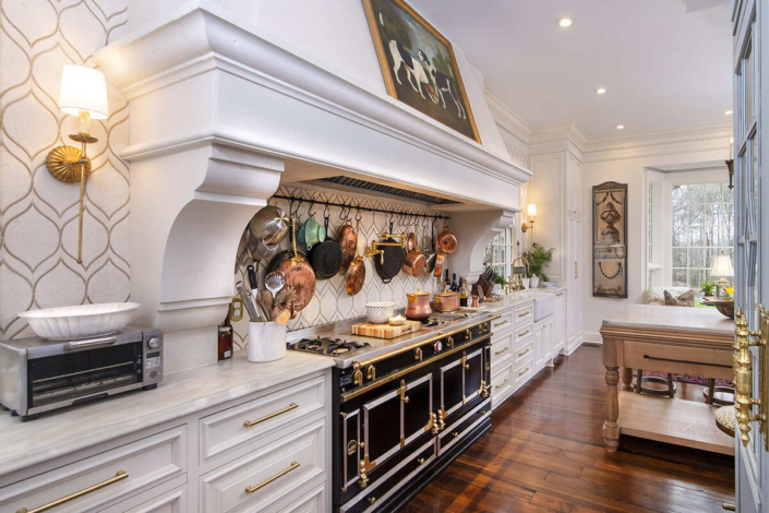 Large white kitchen hood with pot and pan hooks and a large stove