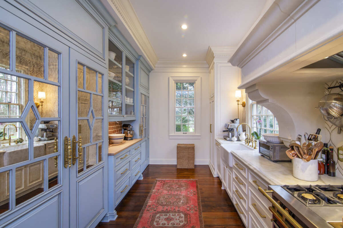 A kitchen with blue and white cabinets with gold hardware and a farmhouse sink