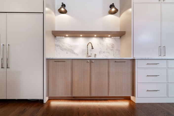 A kitchen with custom cabinets and floating shelves with under cabinet lighting and a sink