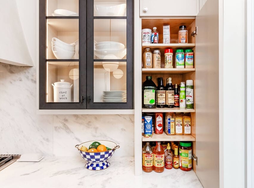 A kitchen with white cabinets and black metal glass doors and a spice storage cabinet