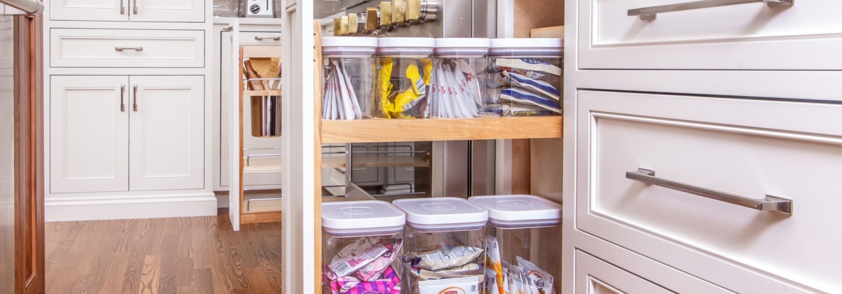A kitchen with a pull out cabinet drawer open showing storage containers neatly inside