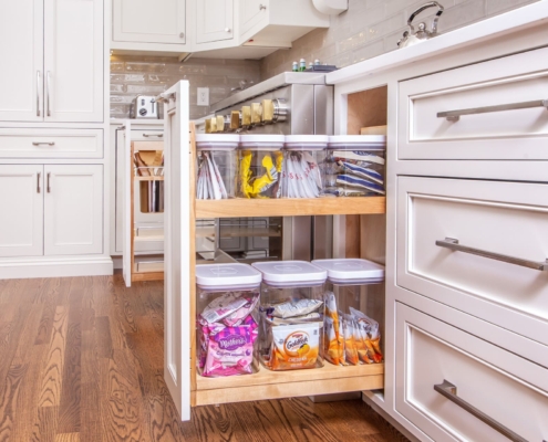 A kitchen with a pull out cabinet drawer open showing storage containers neatly inside