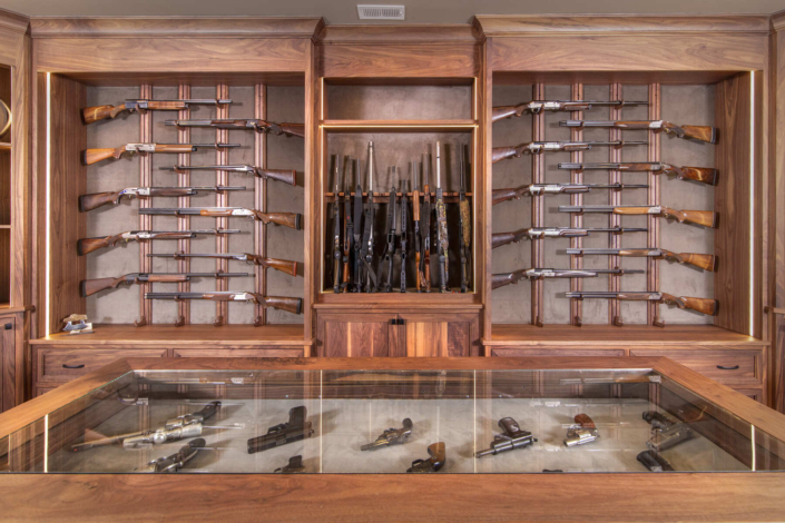A custom gun room with walnut wood cabinets and gun rack displays