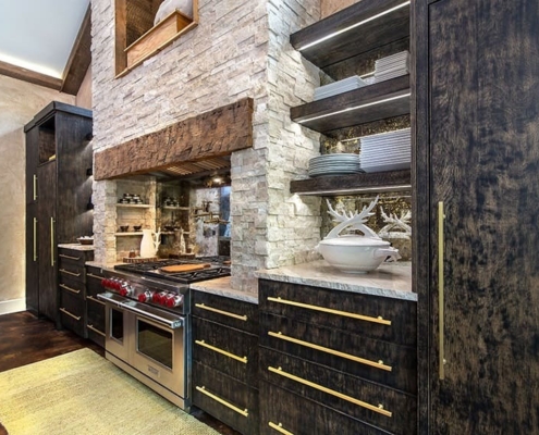 A kitchen with black cabinetry and a stone fireplace above the stove